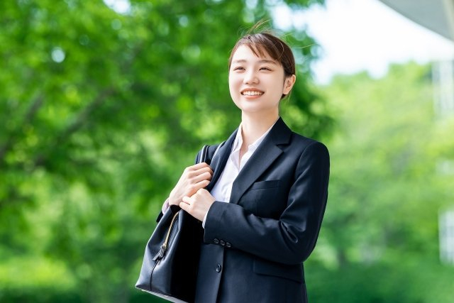 街路樹を背景に笑うスーツ姿の女性